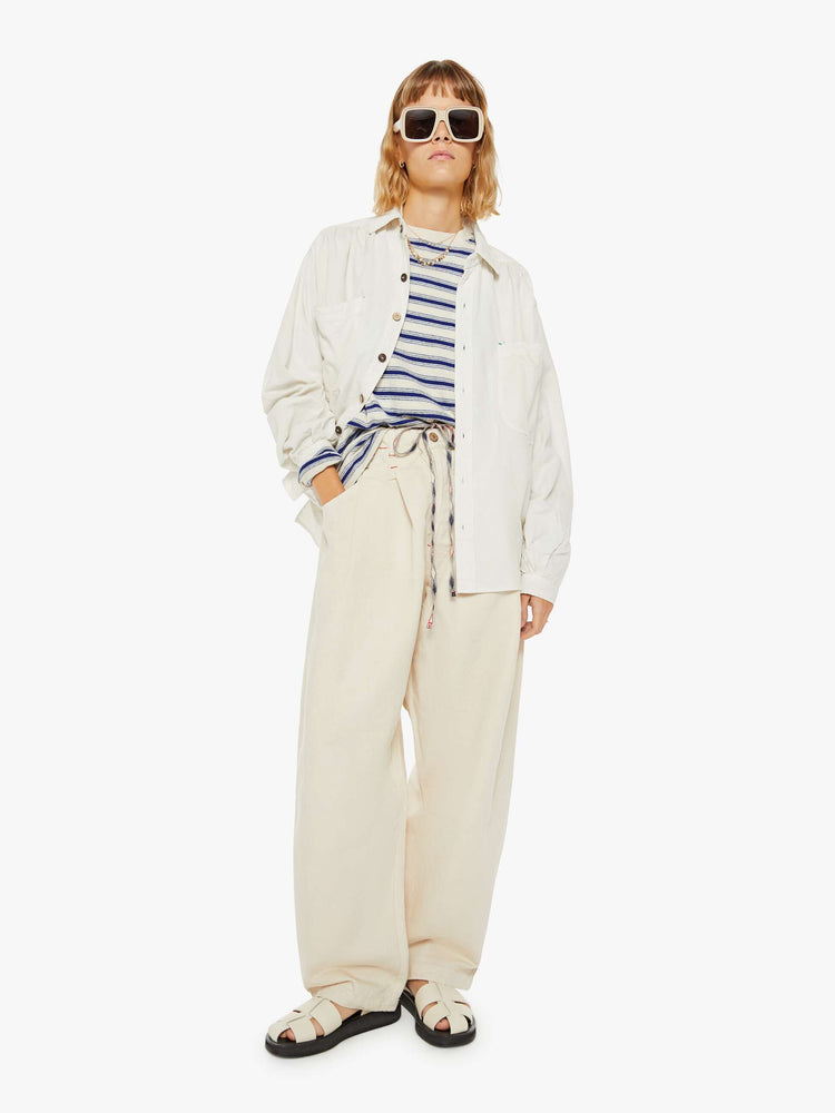 Full body view of a woman off white hue shirt with buttons down the front and a boxy, oversized fit with multi colored buttons.