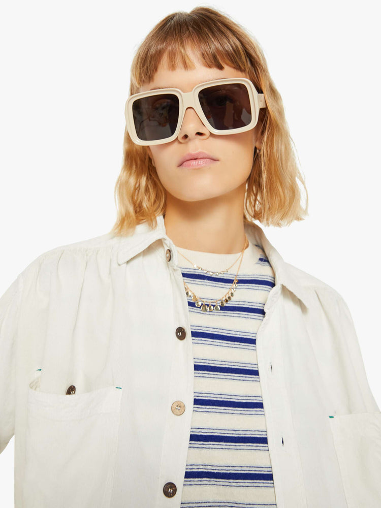 Close up view of a woman off white hue shirt with buttons down the front and a boxy, oversized fit with multi colored buttons.