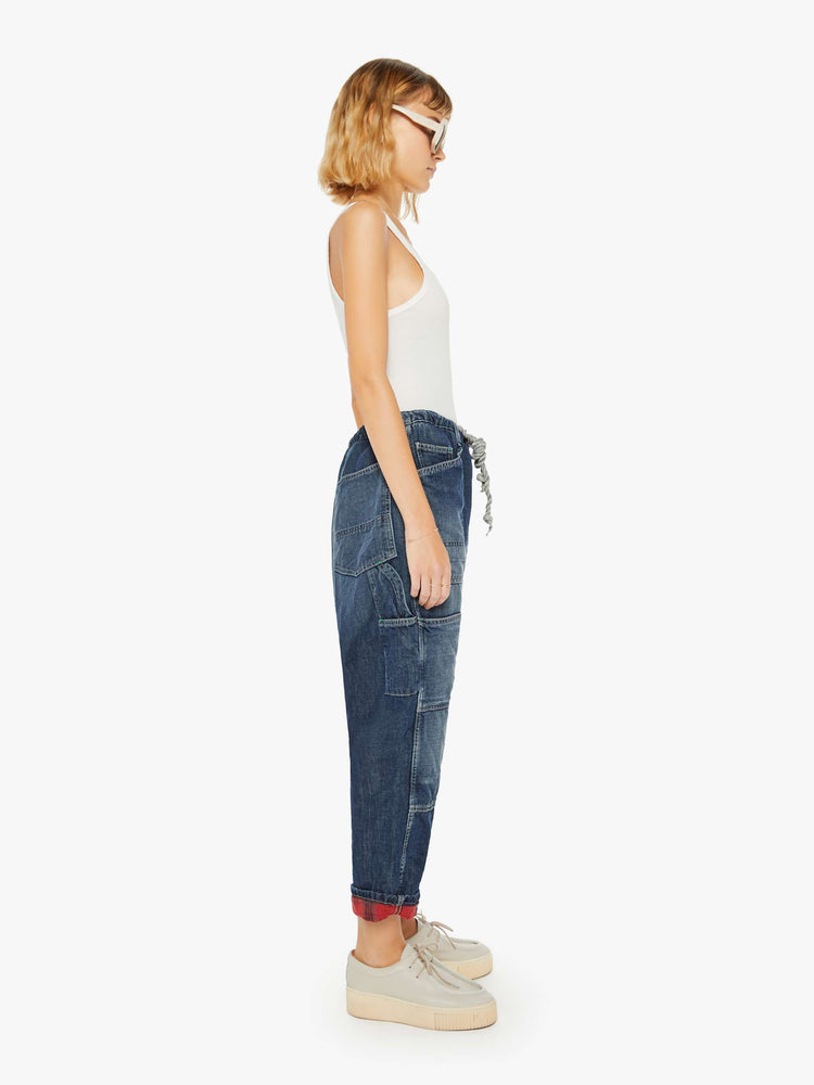 Side view of a woman sunfaded dark wash cargo pants with a mid rise, narrow straight leg and oversized patch pockets throughout.