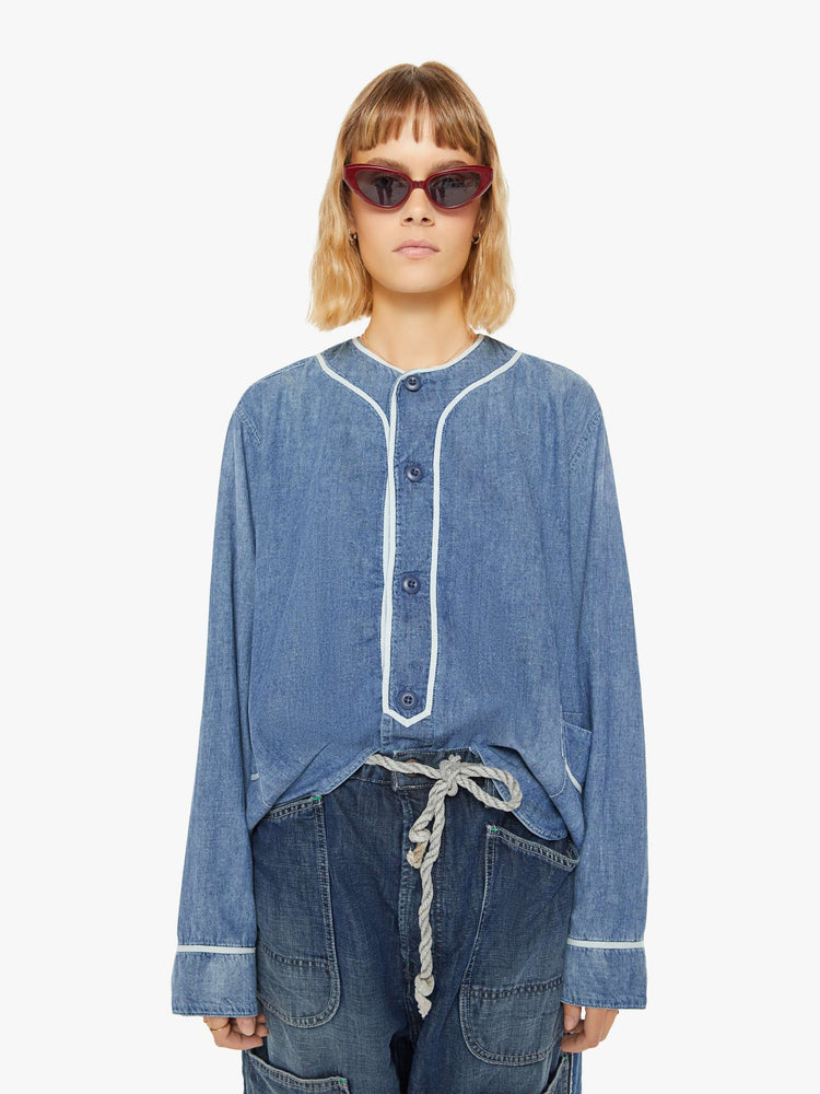 Front view of a woman sun faded indigo hue and long sleeve shirt with a crew neck, extra-long loose sleeves, buttons down the front and an oversized fit.
