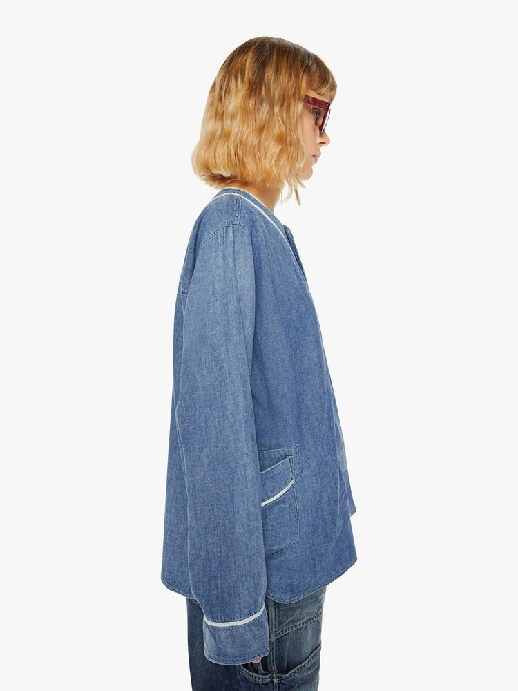 Side view of a woman sun faded indigo hue and long sleeve shirt with a crew neck, extra-long loose sleeves, buttons down the front and an oversized fit.