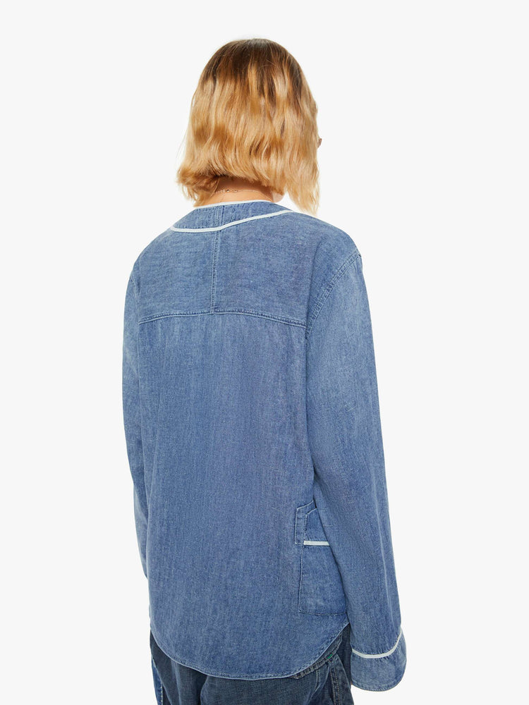 Back view of a woman sun faded indigo hue and long sleeve shirt with a crew neck, extra-long loose sleeves, buttons down the front and an oversized fit.