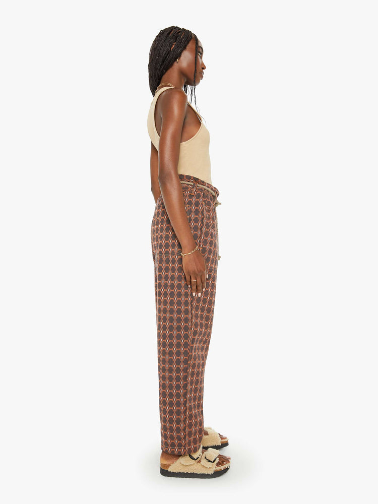 Side view of a woman farmer pant in an orange and brown print with a high rise, straight leg, drawstring waist, a slightly cropped inseam and a loose fit.