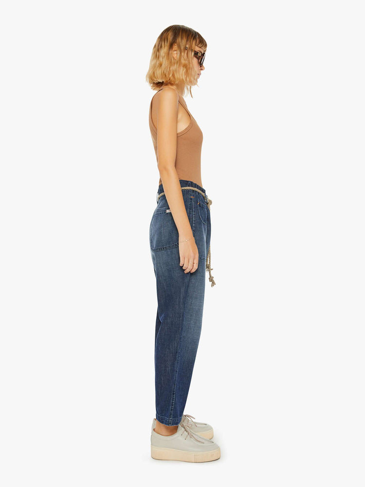 Side view of a woman in pant in a dark blue with a high rise, straight leg, drawstring waist, slightly cropped inseam and loose fit.