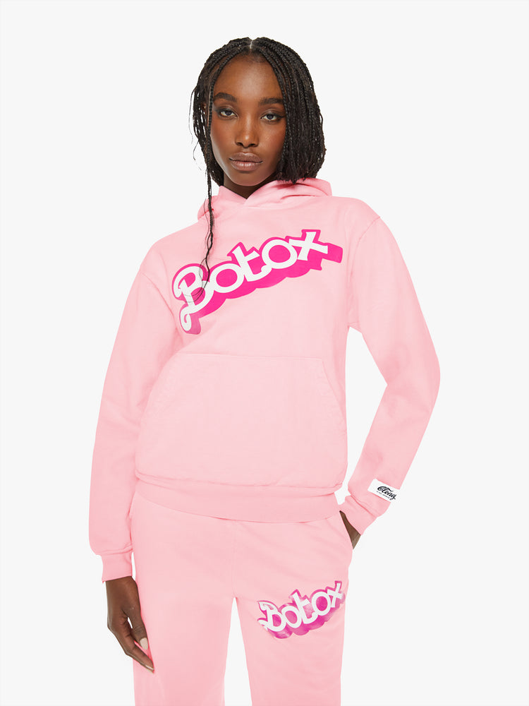 Front view of a woman sweatshirt in baby pink has a front patch pocket, ribbed hems and a slightly oversized fit with a two-toned text graphic on the front.