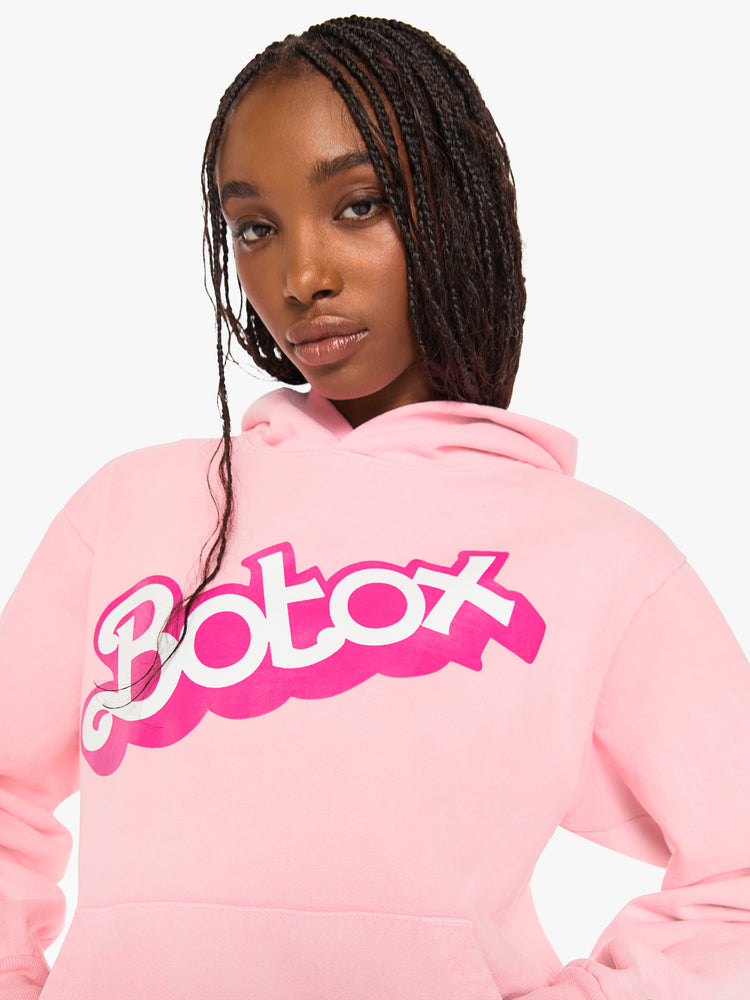 Close up view of a woman sweatshirt in baby pink has a front patch pocket, ribbed hems and a slightly oversized fit with a two-toned text graphic on the front.