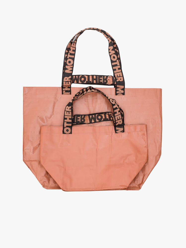 Flat of a dusty pink tote bag with black straps that read "MOTHER".