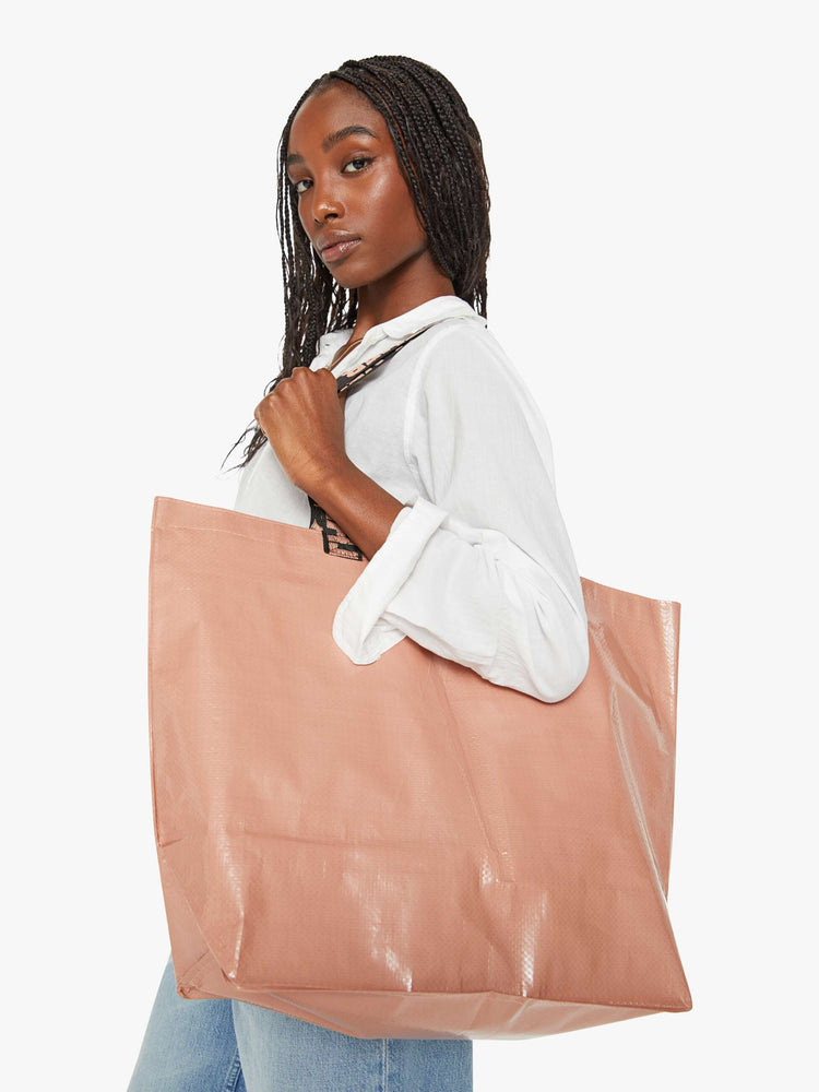 Side view of a woman holding a large dusty pink tote back.