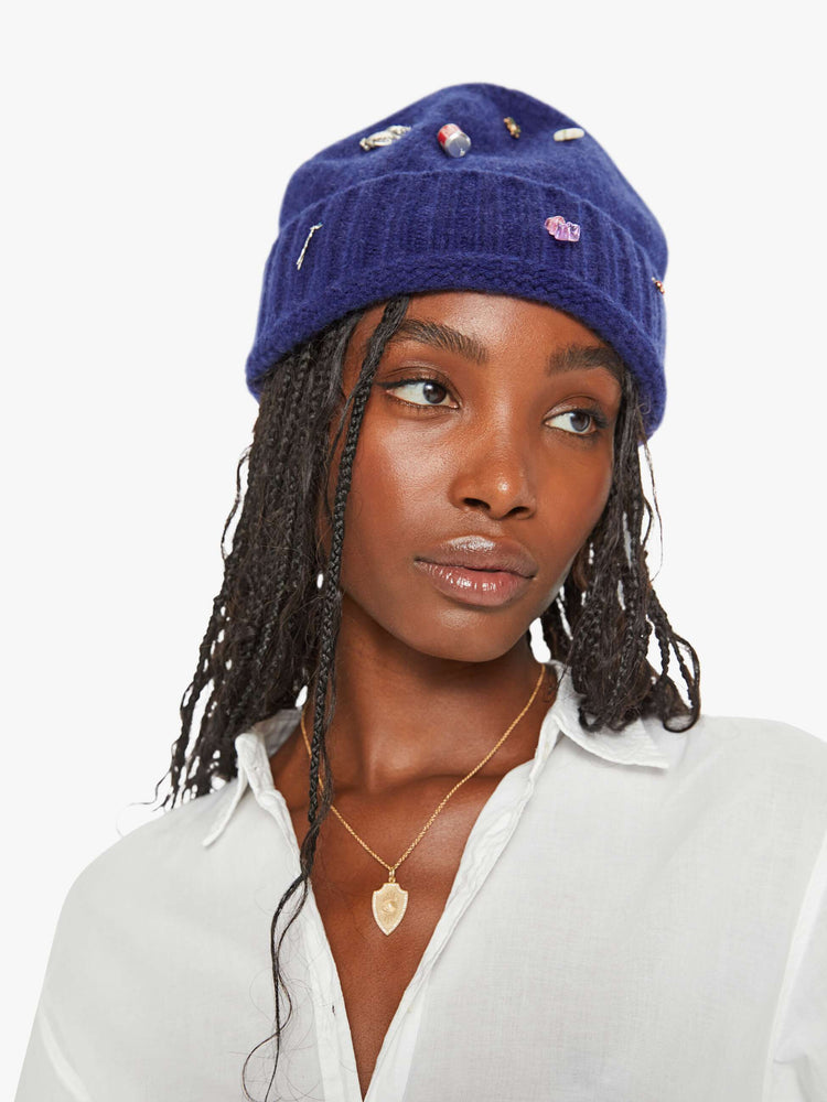A woman wearing a blue knit beanie featuring small assorted charms.