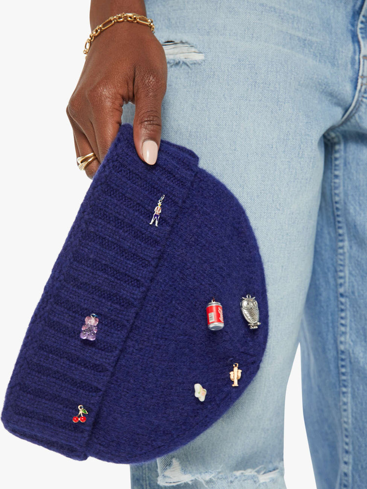 A woman holding a blue knit beanie featuring small assorted charms.