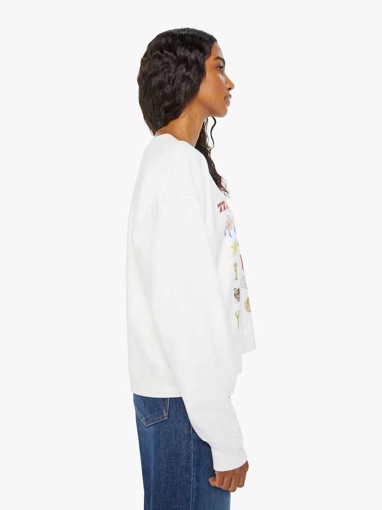 Side view of a woman white long sleeve sweatshirt features a colorful hand-drawn graphic with a variety of good luck charms.