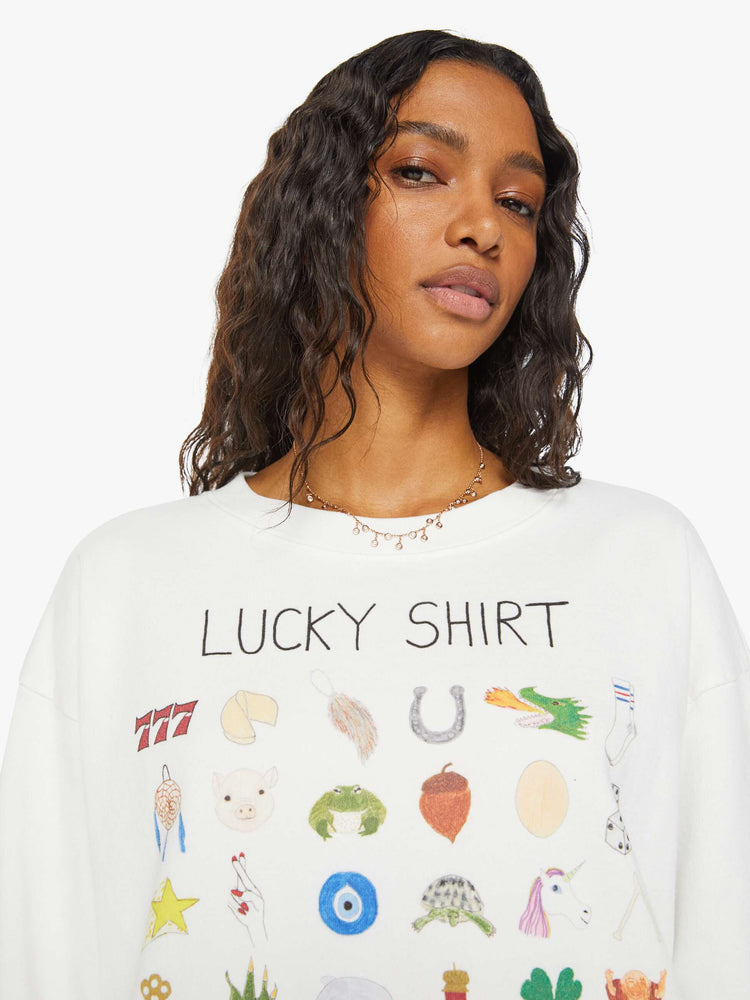 Close up view of a woman white long sleeve sweatshirt features a colorful hand-drawn graphic with a variety of good luck charms.