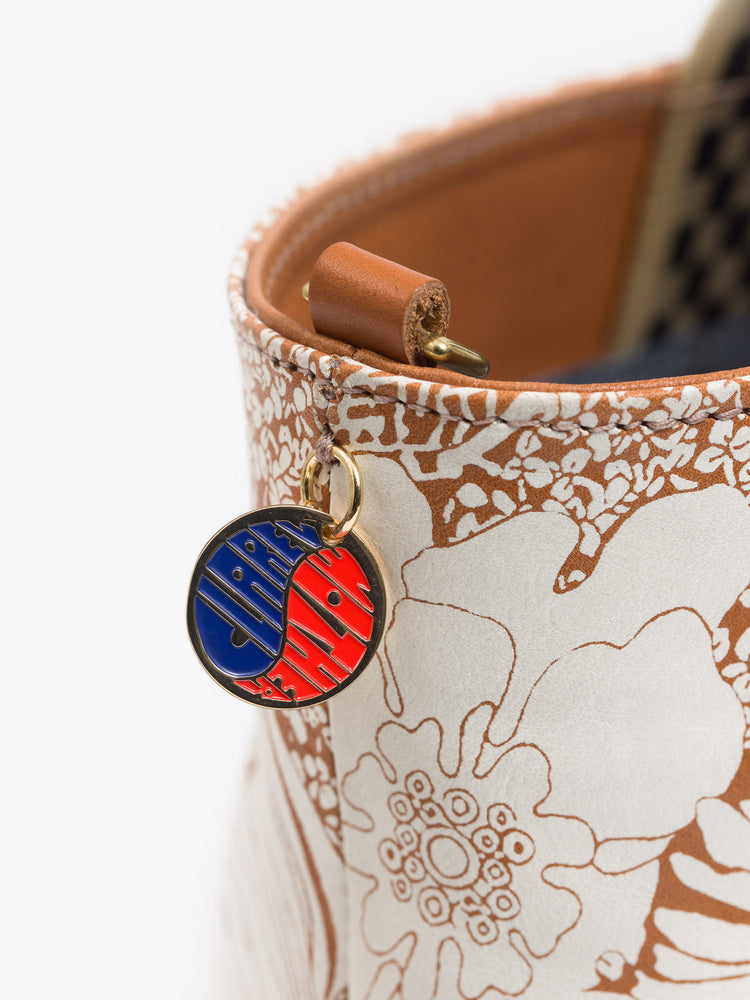 Close up view of a brown and white purse featuring a small round yin and yang charm in gold, blue and red.