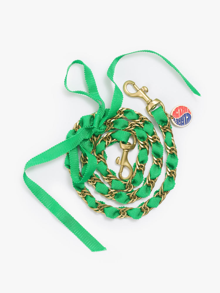 Flat view of a brass chain shoulder strap is detailed with a green ribbon and a small charm.