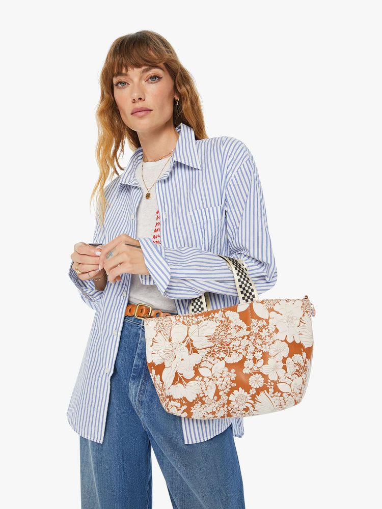 On model view of a rectangular bag features a zip closure and checkered top handle, and is designed in French Fairy Tale, a brown and white floral print. Pair it with the Link Up strap for added versatility.