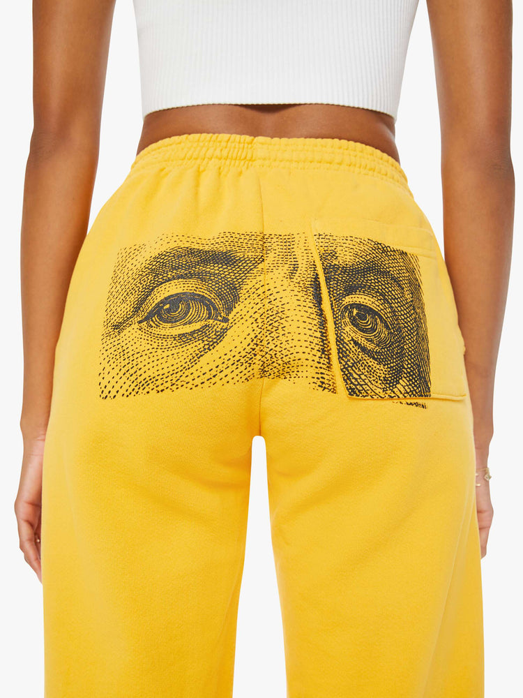 WOMEN back view of a woman mustard yellow elastic waist and cuffs sweatpants with founding fathers eyes on the back.