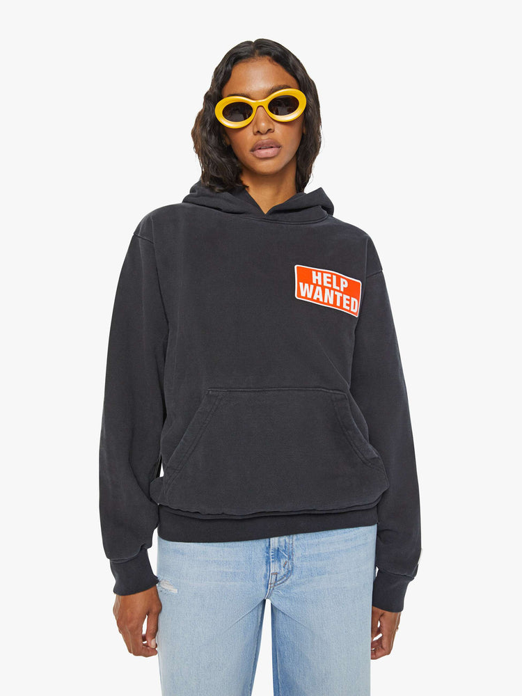 WOMEN front view of black front patch pocket, ribbed hems and a slightly oversized fit sweatshirt with "Help Wanted" graphic and cross on the back.