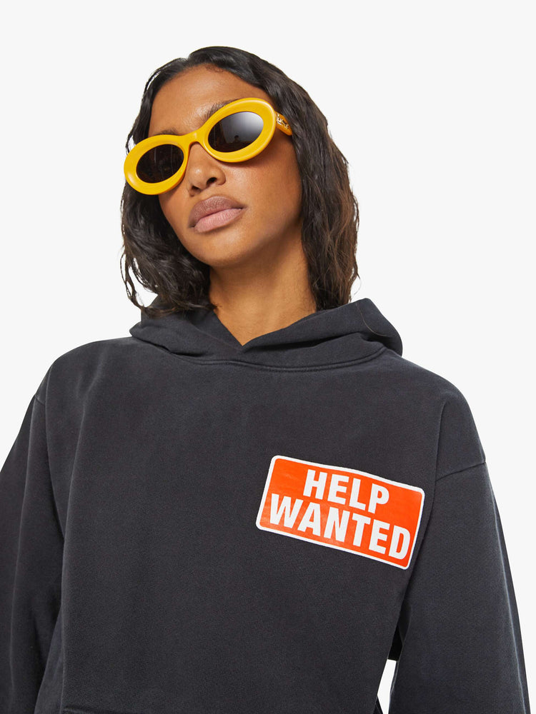 WOMEN close view of black front patch pocket, ribbed hems and a slightly oversized fit sweatshirt with "Help Wanted" graphic and cross on the back.