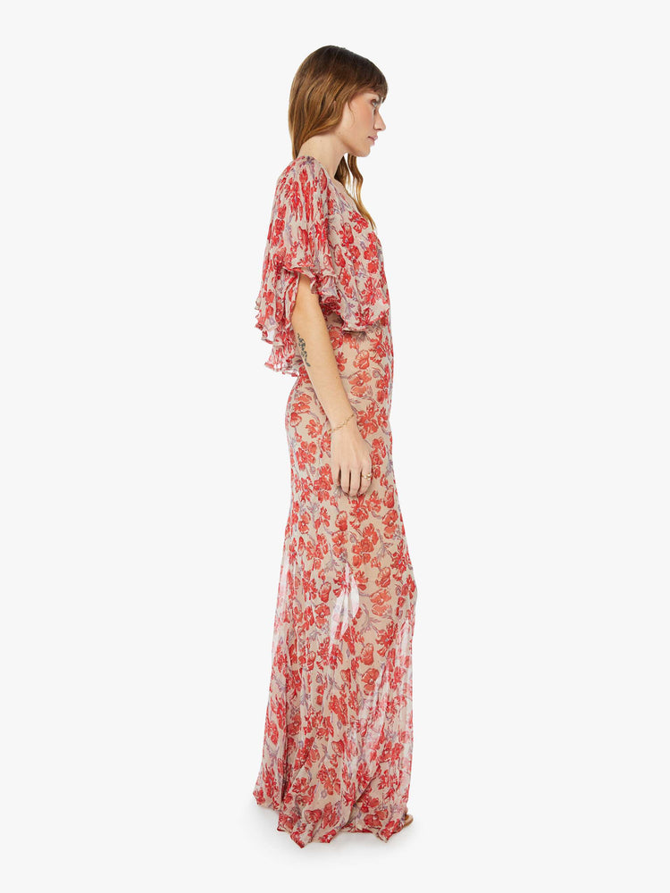 Side view of a floor length flowy dress in a nude and red floral print, featuring a deep v neck and winged sleeves.