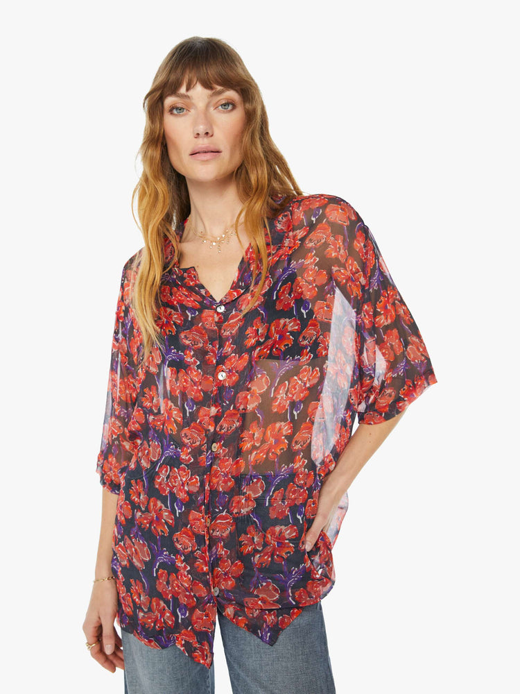 Front view of a woman in a black and red floral print, and features a V-neck, drop shoulders, elbow-length sleeves, buttons down the front and a long, thigh-grazing hem shirt.