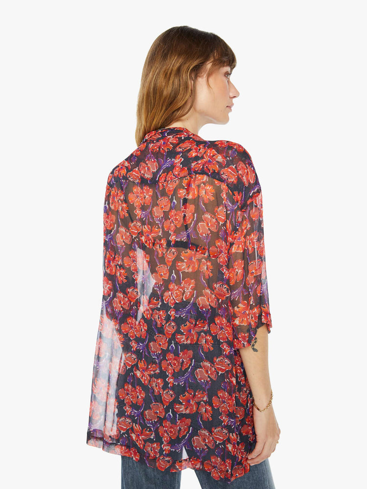 Back view of a woman in a black and red floral print, and features a V-neck, drop shoulders, elbow-length sleeves, buttons down the front and a long, thigh-grazing hem shirt.