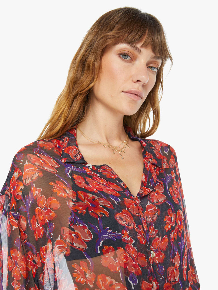Close up view of a woman in a black and red floral print, and features a V-neck, drop shoulders, elbow-length sleeves, buttons down the front and a long, thigh-grazing hem shirt.