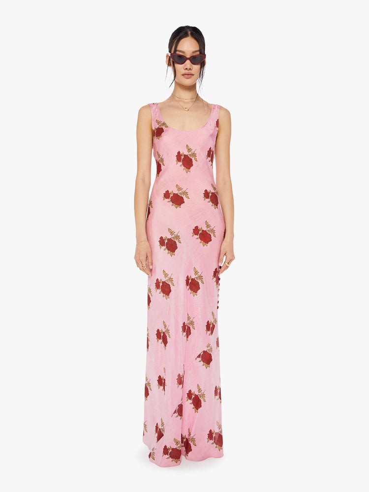 Front view of a woman wearing a pink, sleeveless, maxi dress with red rose print
