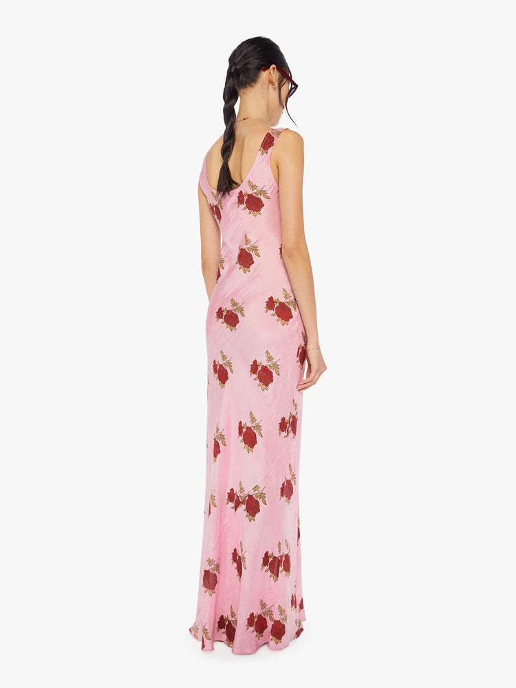 Back view of a woman wearing a pink, sleeveless, maxi dress with red rose print