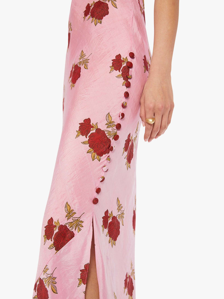 Detail view of a woman wearing a pink, sleeveless, maxi dress with red rose print