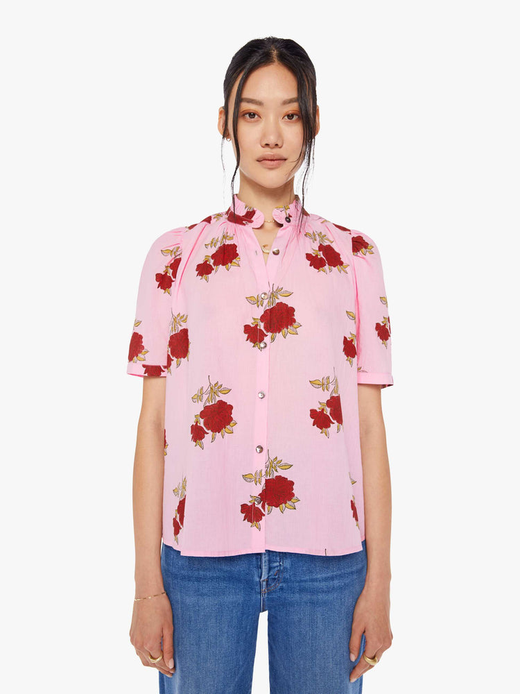 Front view of a woman wearing a pink button up shirt with red rose print, ruffled collar, and short sleeves
