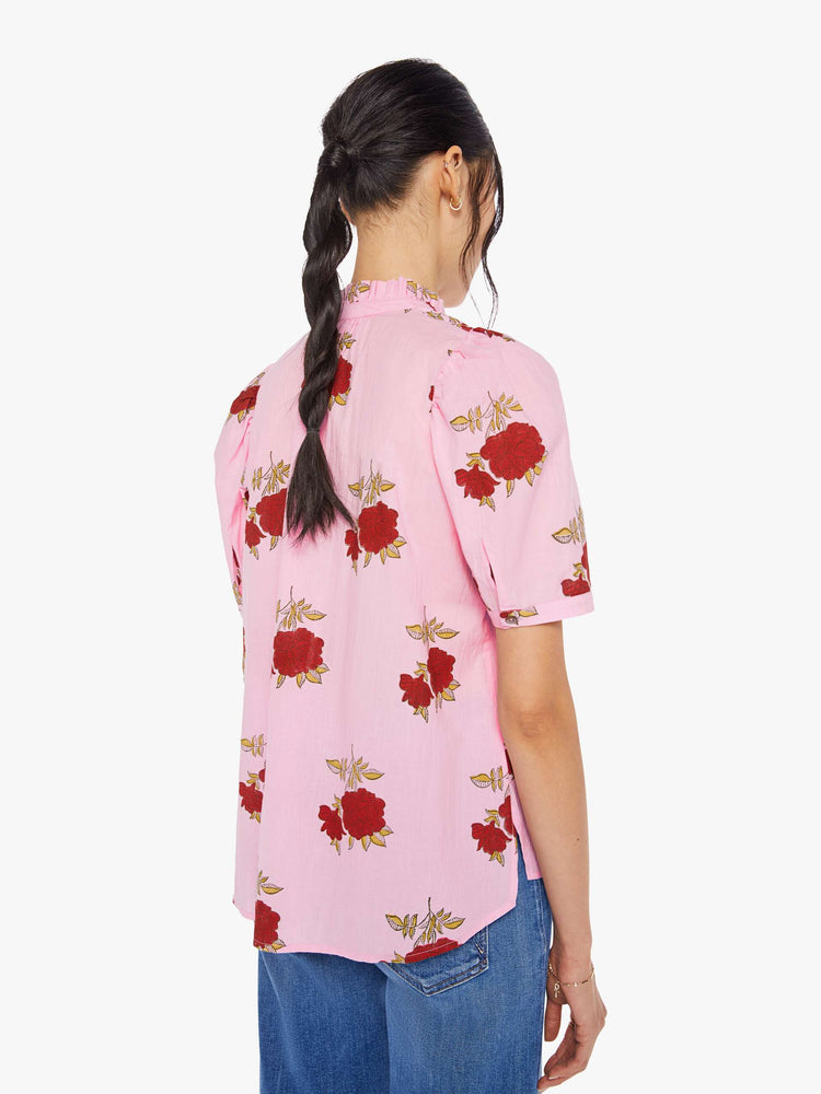 Back view of a woman wearing a pink button up shirt with red rose print, ruffled collar, and short sleeves