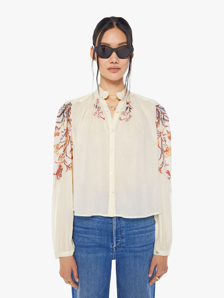 Front view of a woman wearing an off-white, button down blouse with floral print on the collar and sleeves