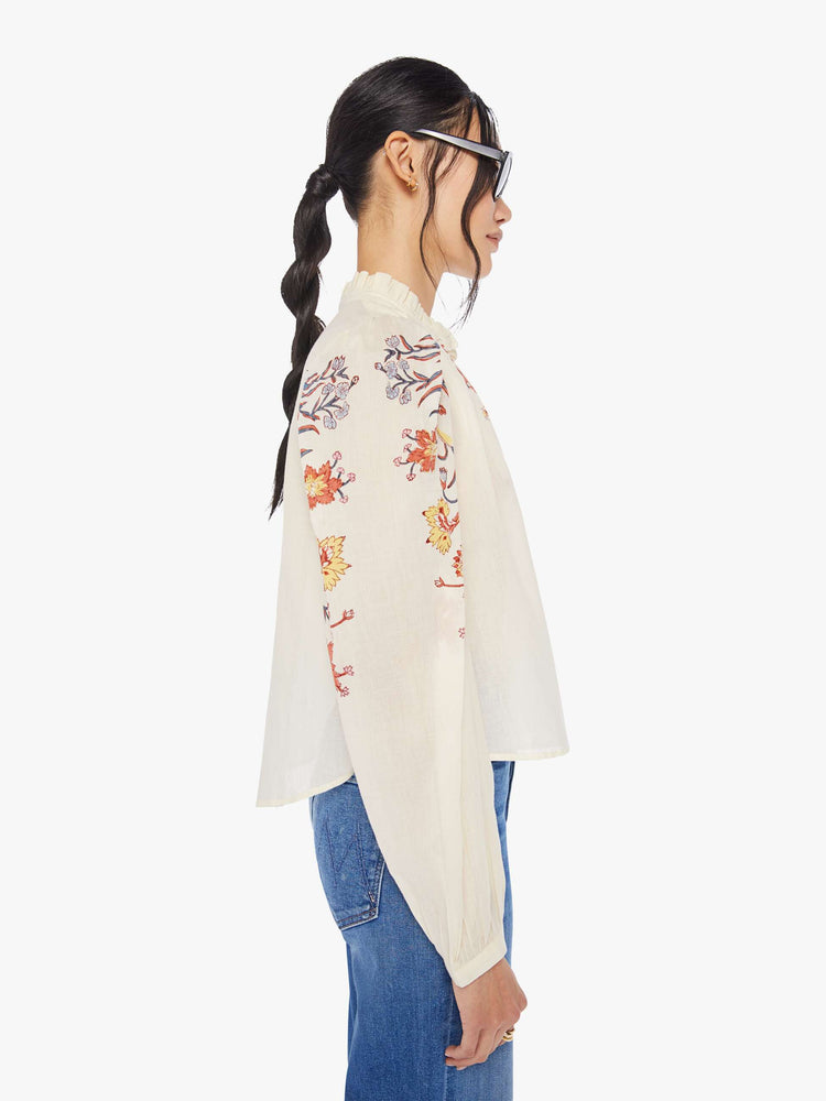 Side view of a woman wearing an off-white, button down blouse with floral print on the collar and sleeves
