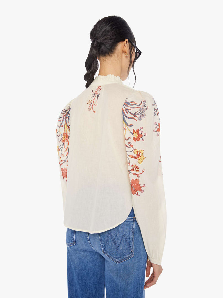 Back view of a woman wearing an off-white, button down blouse with floral print on the collar and sleeves