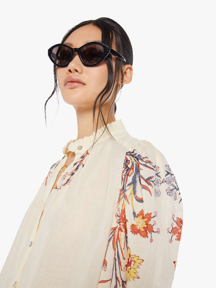 Detail view of a woman wearing an off-white, button down blouse with floral print on the collar and sleeves