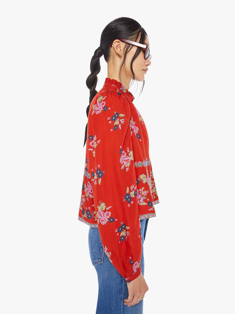 Side view of a woman wearing a red, button down blouse with floral print and balloon sleeves