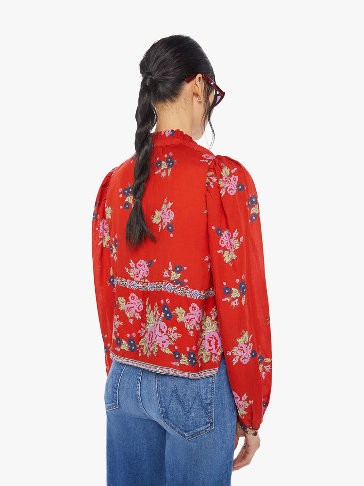 Back view of a woman wearing a red, button down blouse with floral print and balloon sleeves
