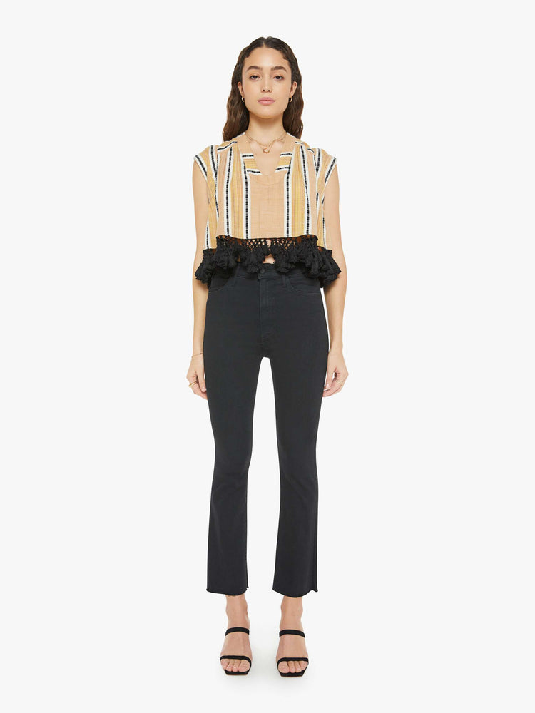 Front full body view of a woman wearing a yellow, striped button up top with black lace fringe at the hem
