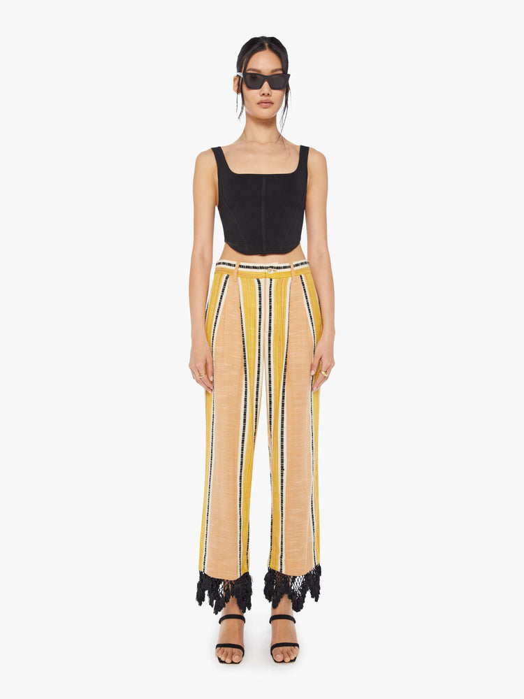 Front view of a woman wearing yellow striped pants with black lace fringe detail at the hem