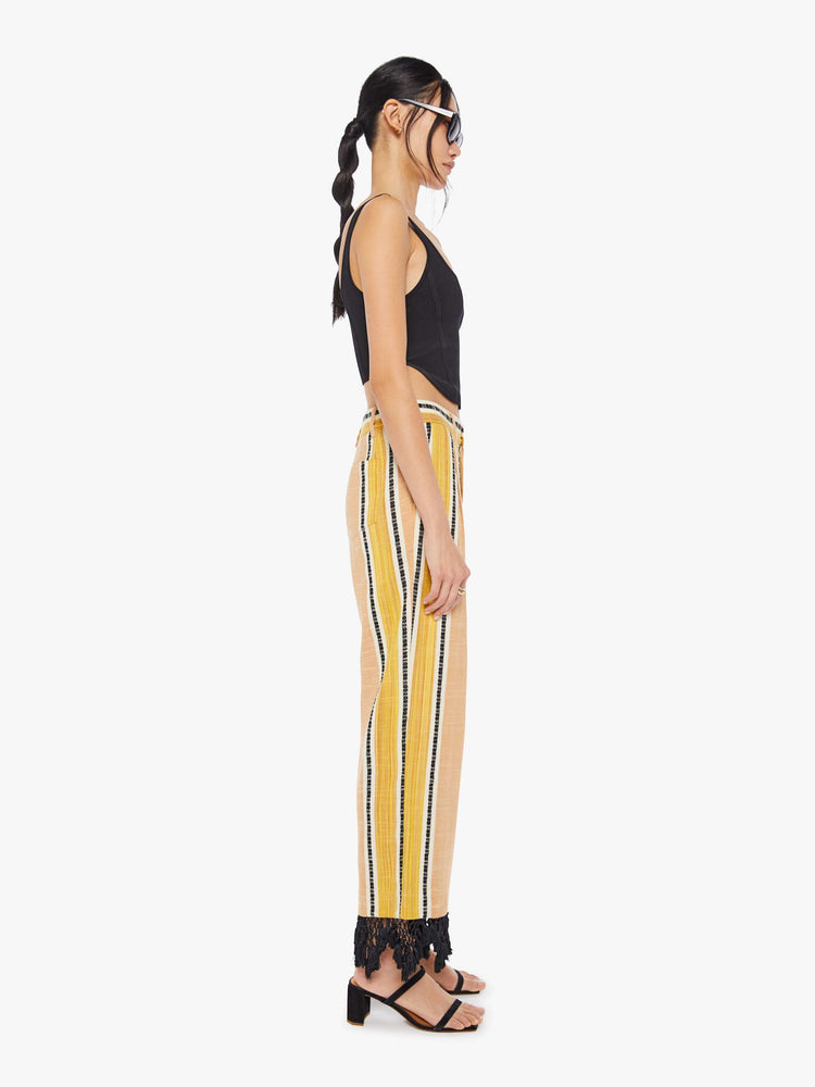 Side view of a woman wearing yellow striped pants with black lace fringe detail at the hem