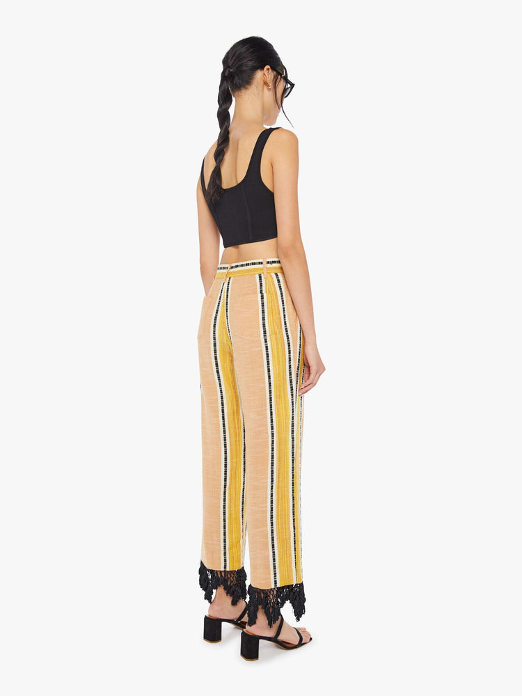 Back view of a woman wearing yellow striped pants with black lace fringe detail at the hem