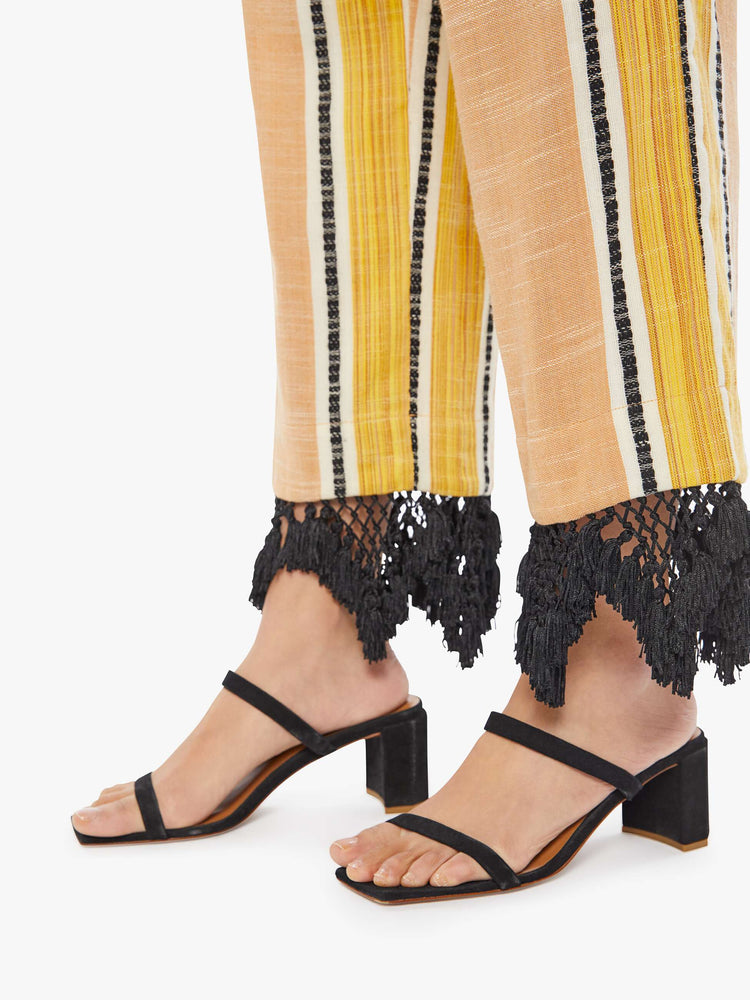 Detail view of a woman wearing yellow striped pants with black lace fringe detail at the hem
