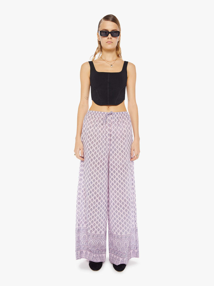 Front view of a woman wearing loose cotton pants with all-over purple floral print and drawstring waist