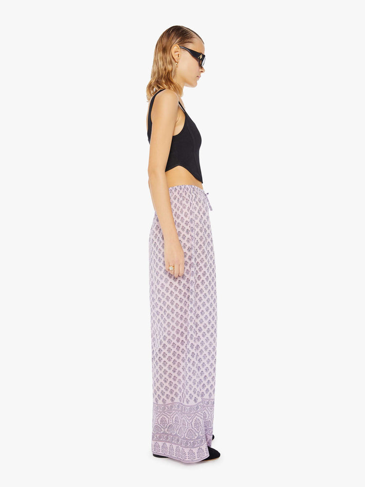 Side view of a woman wearing loose cotton pants with all-over purple floral print and drawstring waist