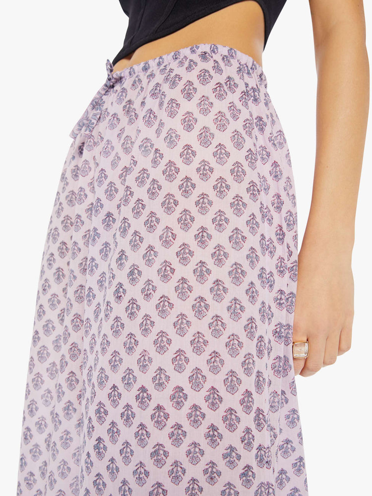 Detail view of a woman wearing loose cotton pants with all-over purple floral print and drawstring waist