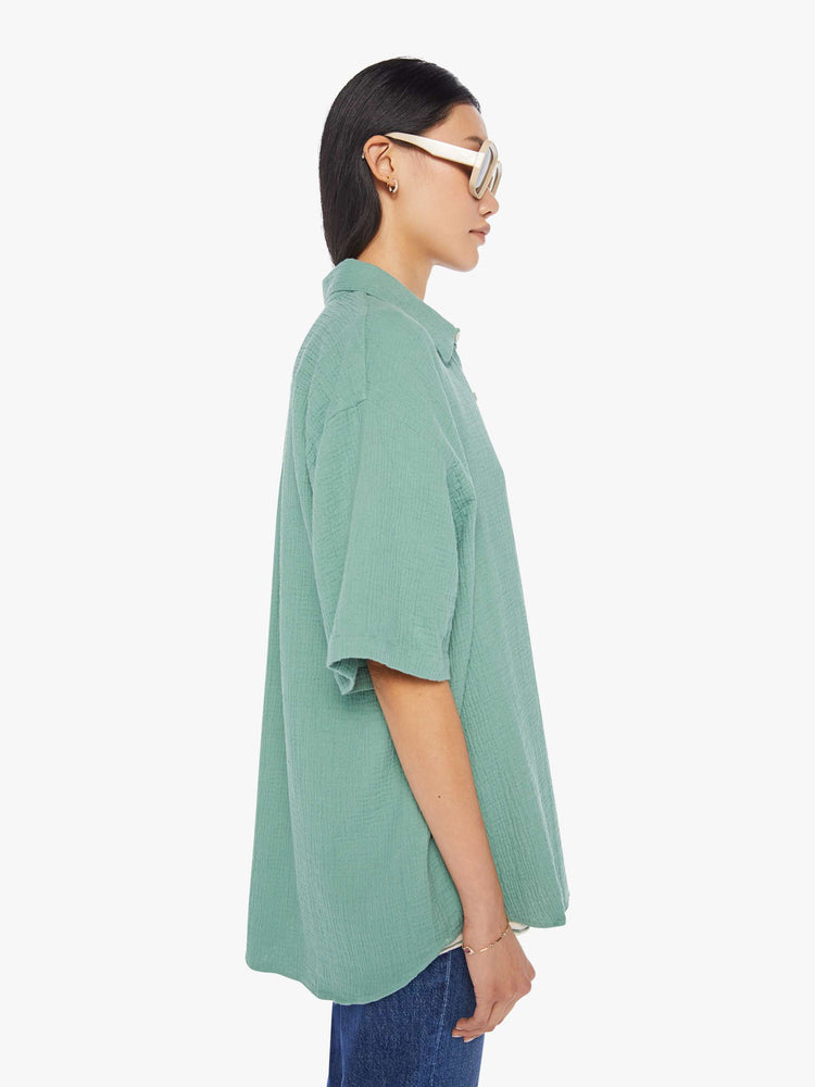 Side view of a womens green short sleeve button down shirt featuring an oversized fit.