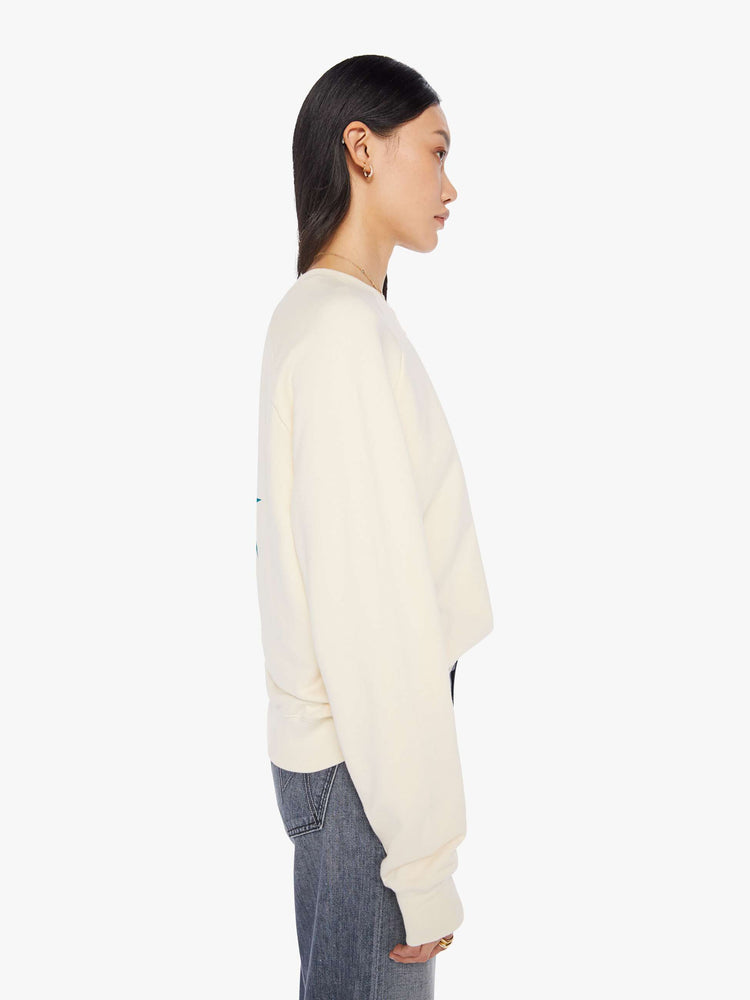 Side view of a womens ecru crew neck sweatshirt featuring an oversized fit and a logo printed on the chest pocket.
