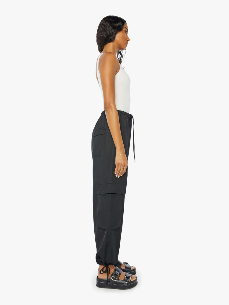 Side view of a woman wearing a black cargo pant with an elastic tie waist and hem, large side pockets, paired with a white tank top.