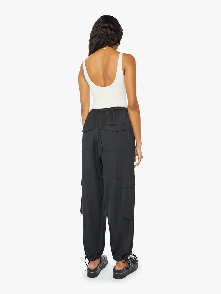 Back view of a woman wearing a black cargo pant with an elastic tie waist and hem, large side pockets, paired with a white tank top.