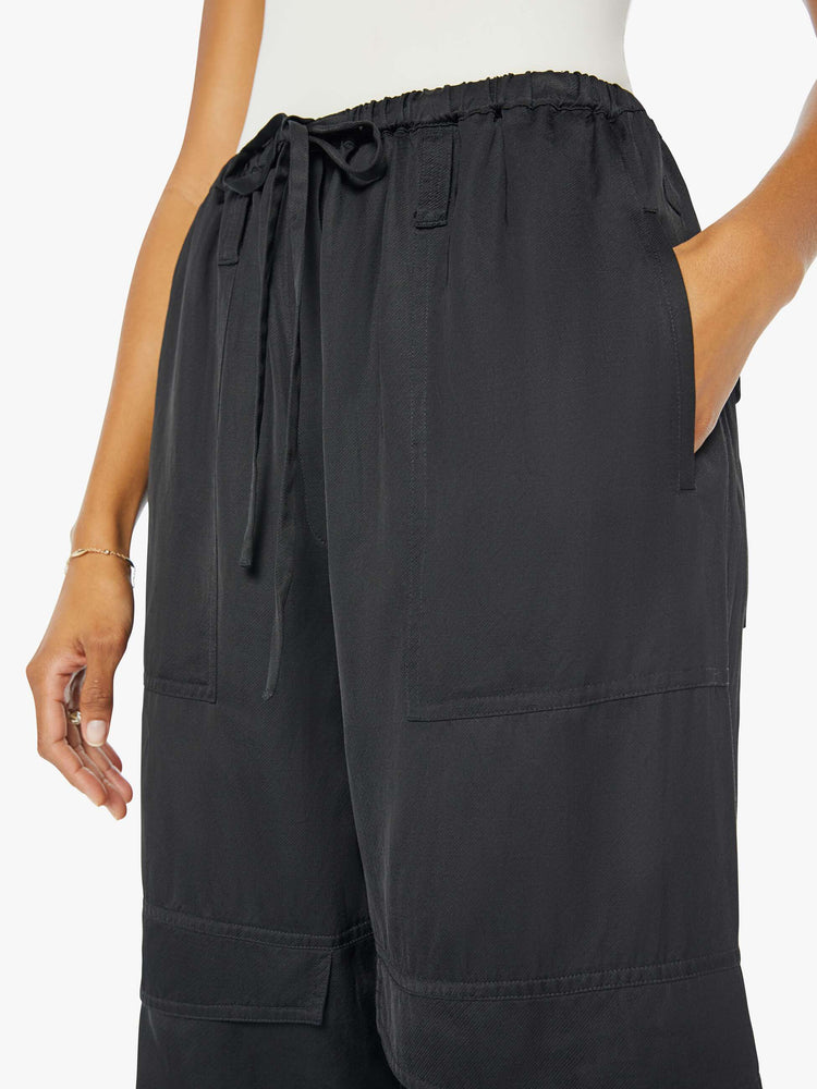 Front close up view of a woman wearing a black cargo pant with an elastic tie waist and hem, large side pockets, paired with a white tank top.
